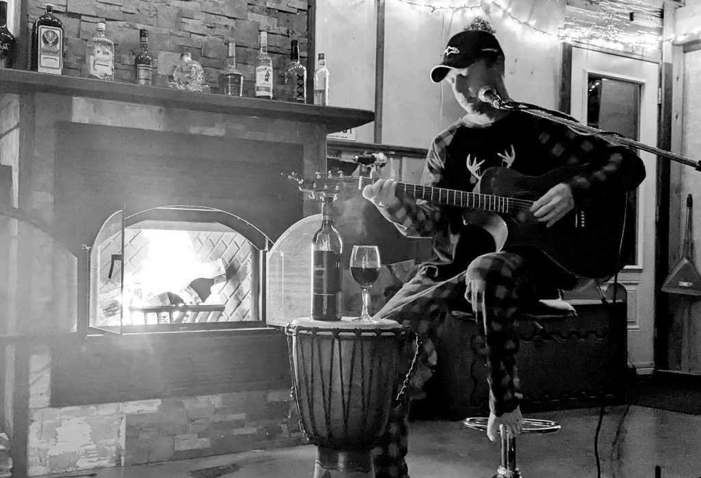 c-bas assis sur un tabouret avec sa guitare déposé sur lui, image en noir et blanc.
