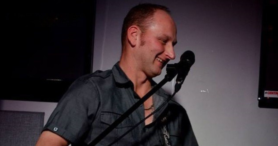 luc st martin sur scène qui chante, un micro devant lui et une guitare à la main