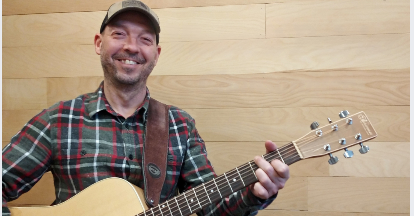 Vincent Poirier debout et souriant tenant sa guitare